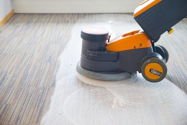 Orangene Wischmaschine bei der Reinigung eines bunten Teppichbodens..